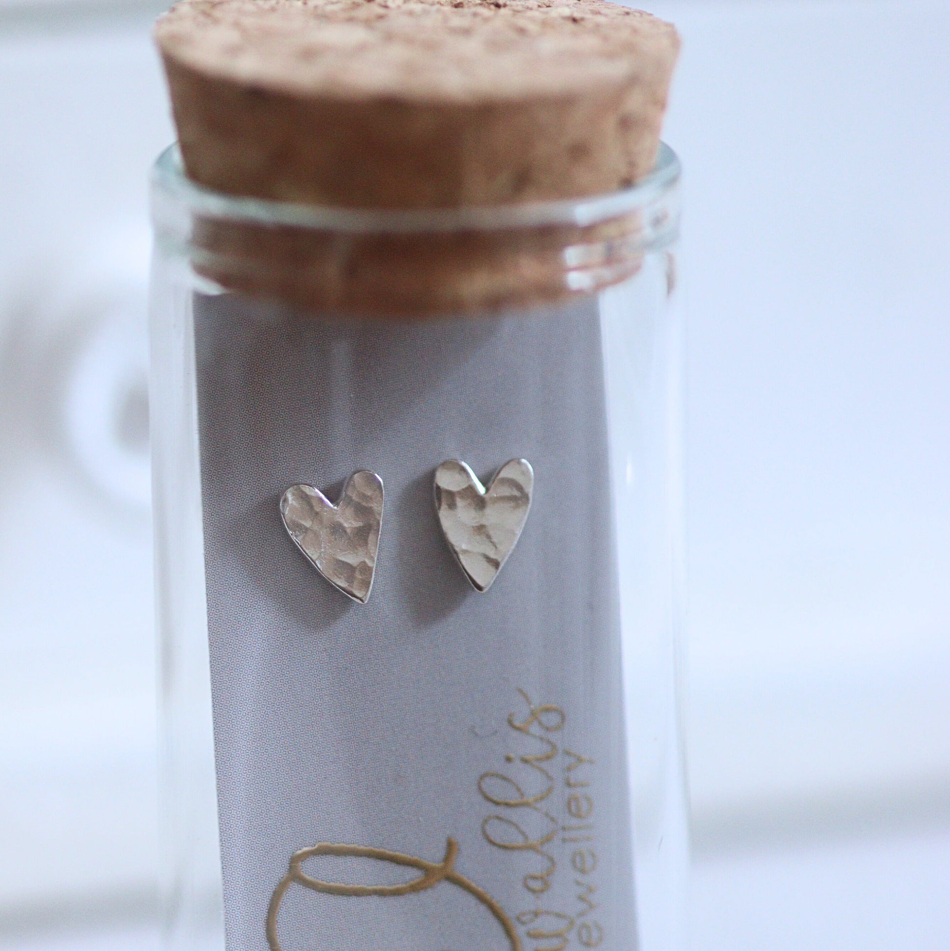 Silver heart earrings in a glass jar with cork lid on a white background