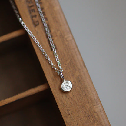 Silver chain with a personalised round pendant on a wooden surface
