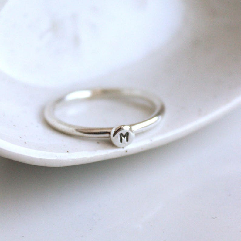 Silver stacking ring with a round dot and initial stamped on it.