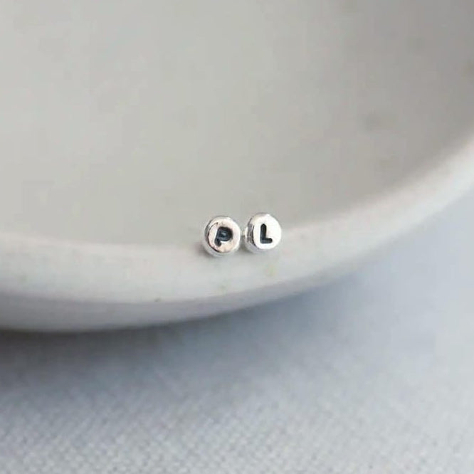Silver stud earrings with initials on a light grey background