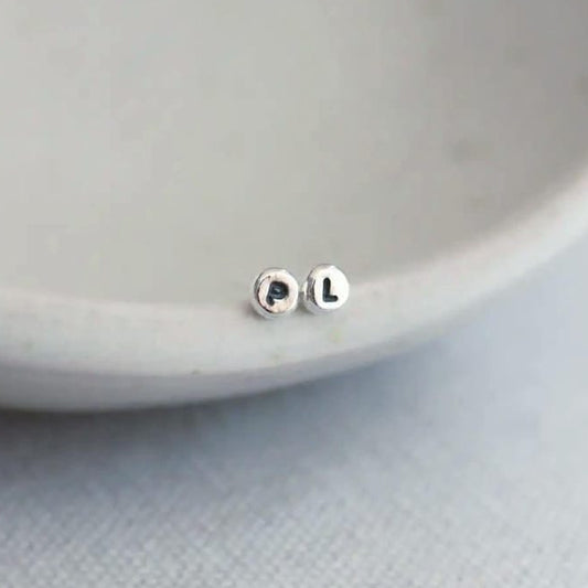Silver stud earrings with initials on a light grey background