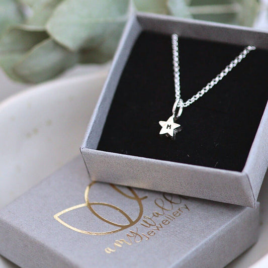 Silver star charm on a fine silver chain with a letter m personalisation. In a grey branded box.