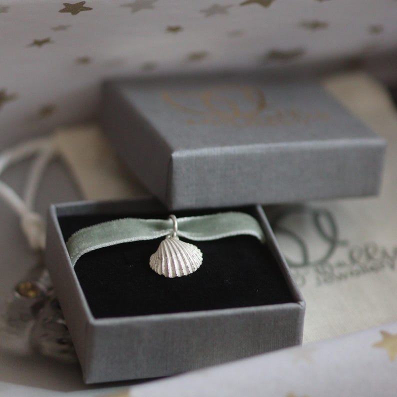 Silver seashell pendant in a grey jewellery box with star-patterned tissue paper