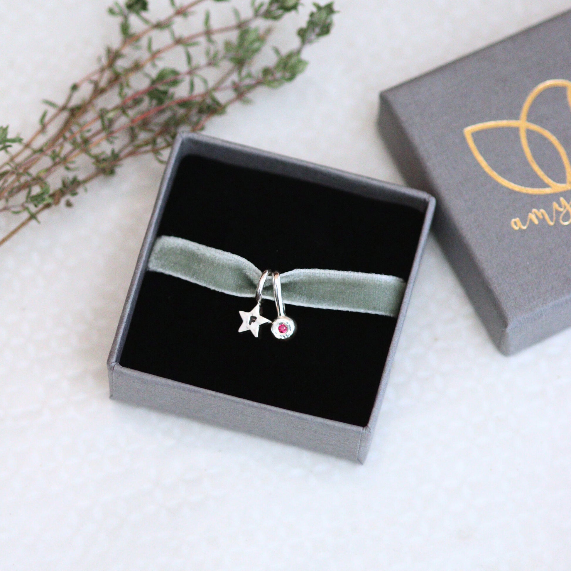 silver star charm on a green velvet ribbon in a jewellery box on a light background.