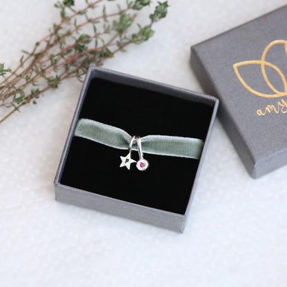 silver star charm on a green velvet ribbon in a jewellery box on a light background.