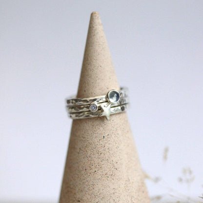 Three silver rings with gemstones and stars on a textured cone-shaped stand against a light background