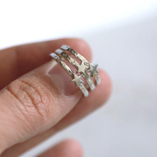 Silver stacking ring with star design on a finger against a white background