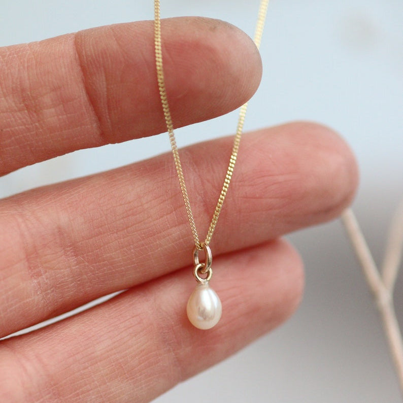 Minimalist Gold fine chain necklace with a pearl pendant held between fingers against a neutral background