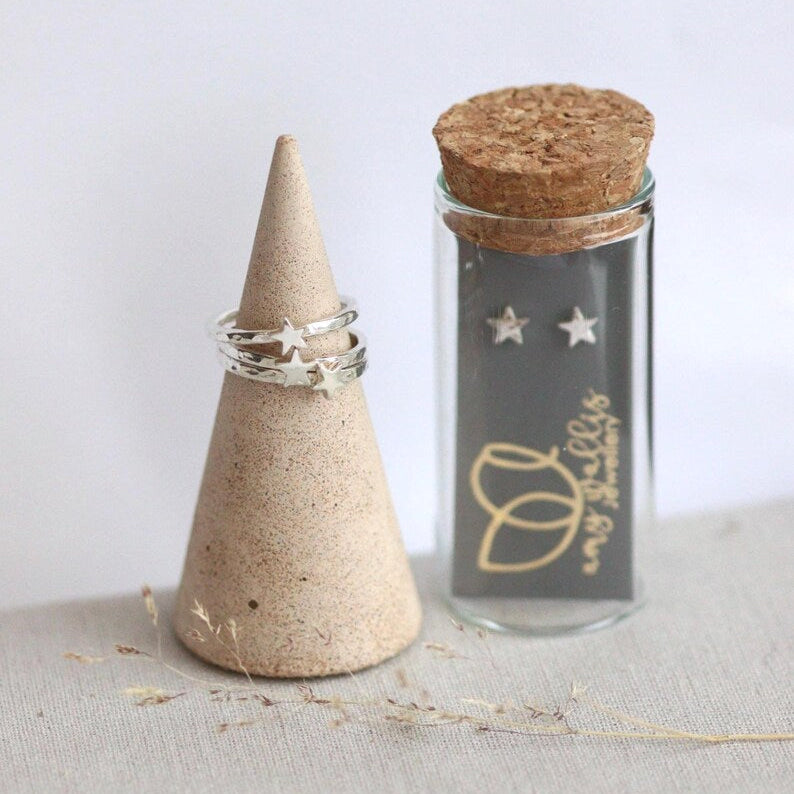 Cork lidded glass tube with silver star shaped studs inside and silver star stacking rings on a ring cone.