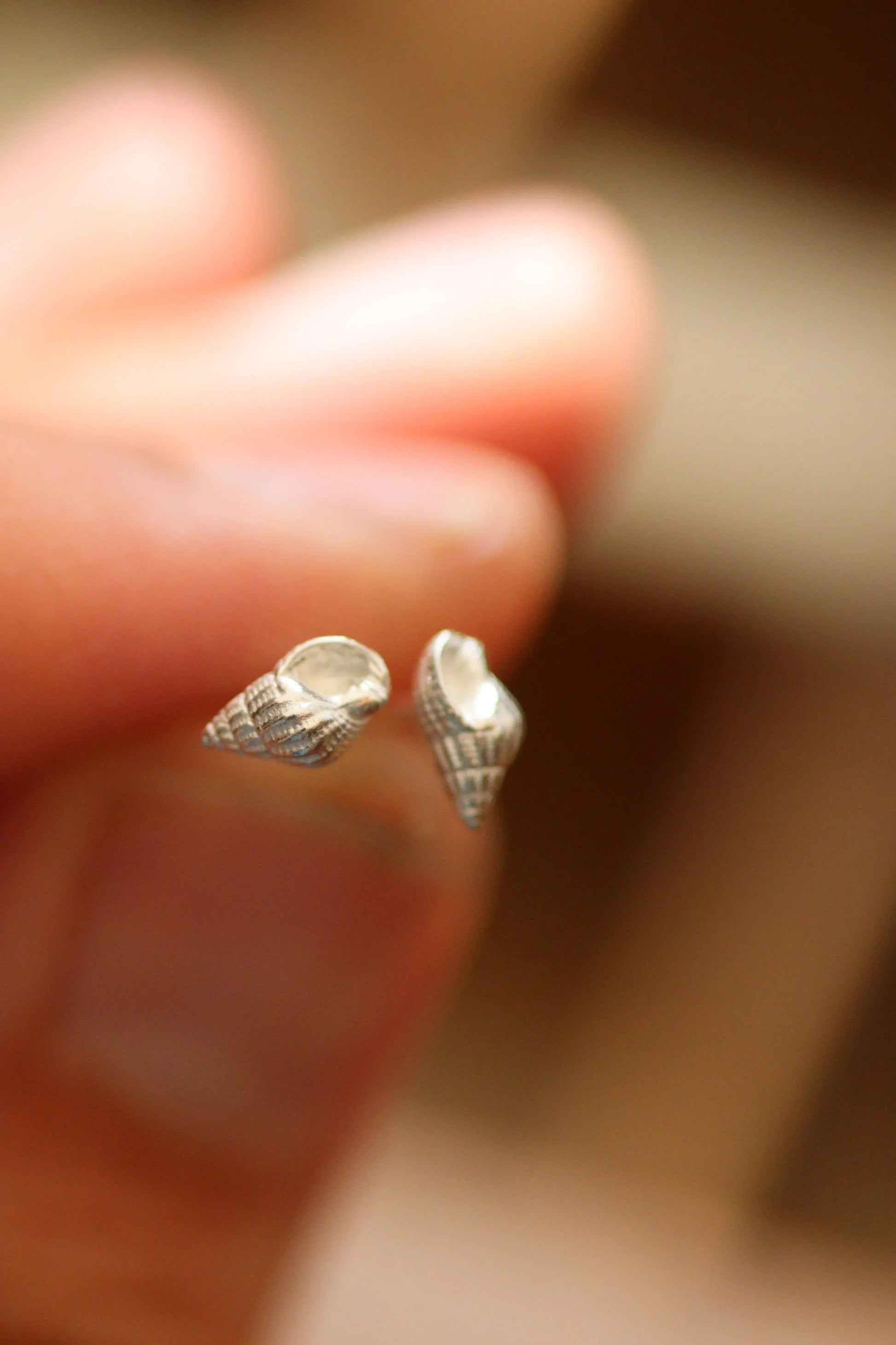 Silver shell-shaped earrings held between fingers with a blurred background.