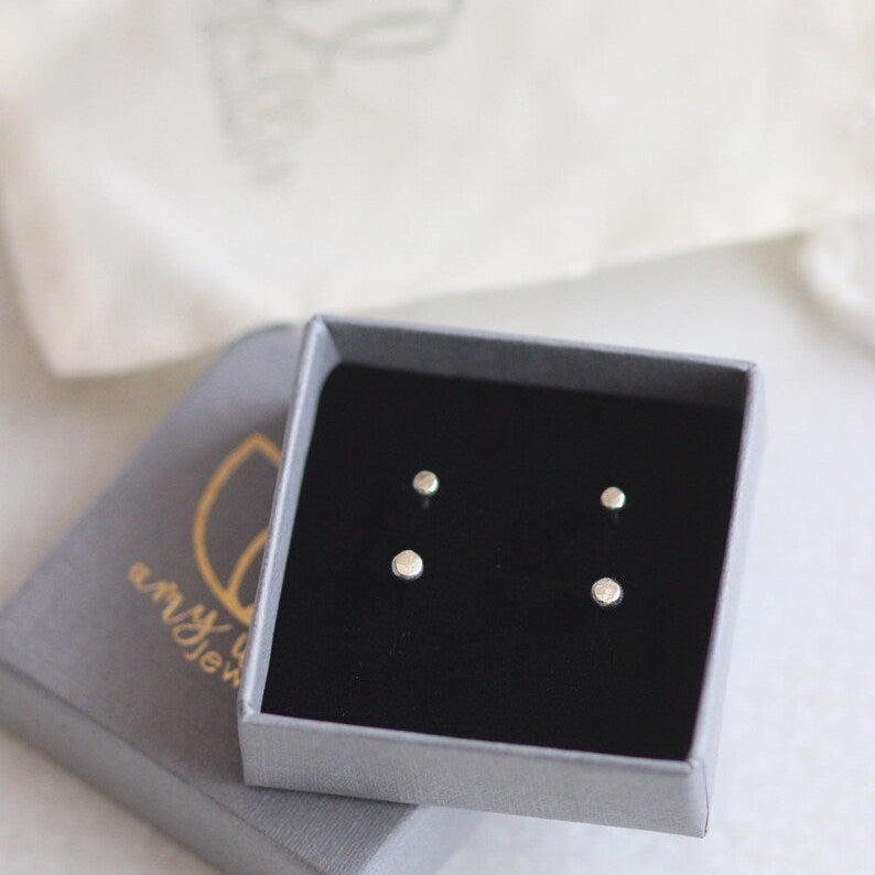 Two pairs of gold stud earrings in a grey jewellery box and cotton pouch