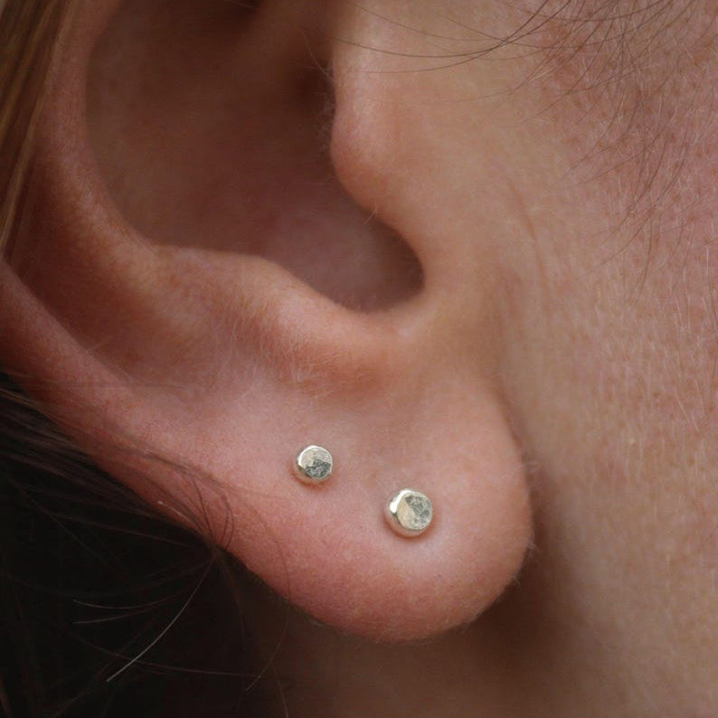 Close-up of an ear wearing two small  white gold stud earrings.