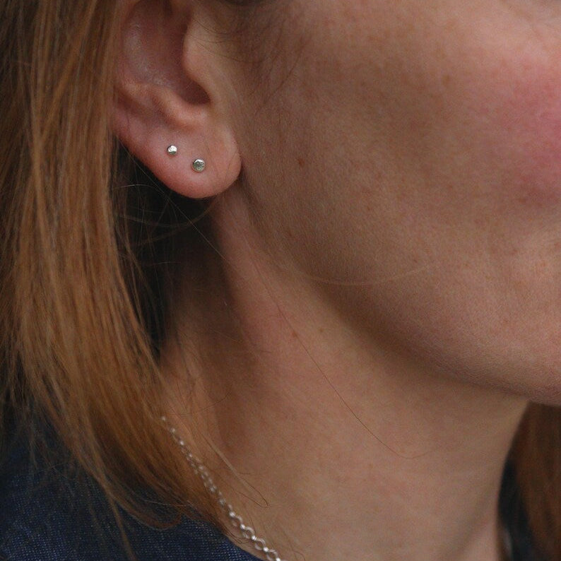 Close-up of a person wearing white gold tiny dot earrings one larger than the other 3mm and 2.5mm