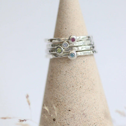 Stack of silver rings with colourful gemstones on a textured cone-shaped stand against a light background
