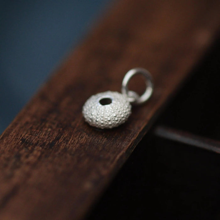 A silver urchin charm on a dark wooden tray.