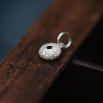 A silver urchin charm on a dark wooden tray.