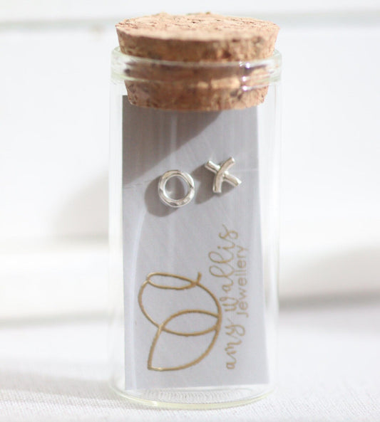 Silver stud earrings in a glass bottle with cork top. A circle hug and a cross kiss stud.