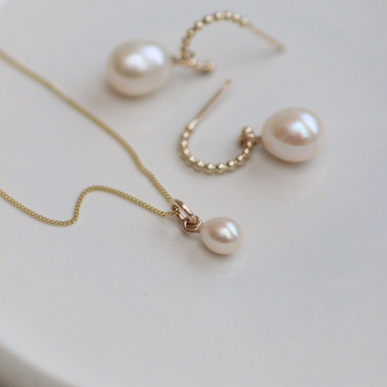 Gold Pearl drop necklace and gold hoop earrings on a white surface