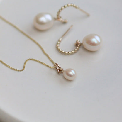 Gold Pearl drop necklace and gold hoop earrings on a white surface