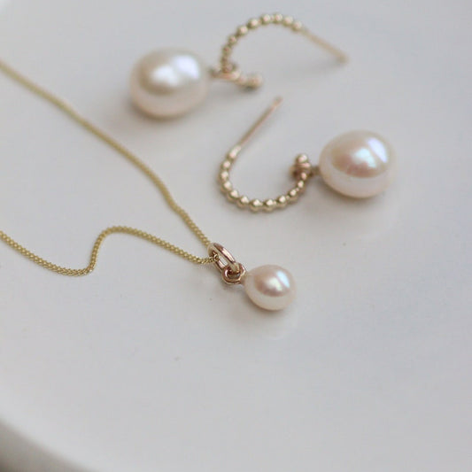 Gold Pearl drop necklace and gold hoop earrings on a white surface