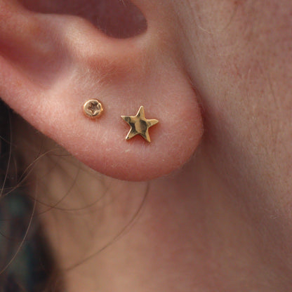 Tiny gold star studs in an ear lobe with tiny star dots in the second piercing.