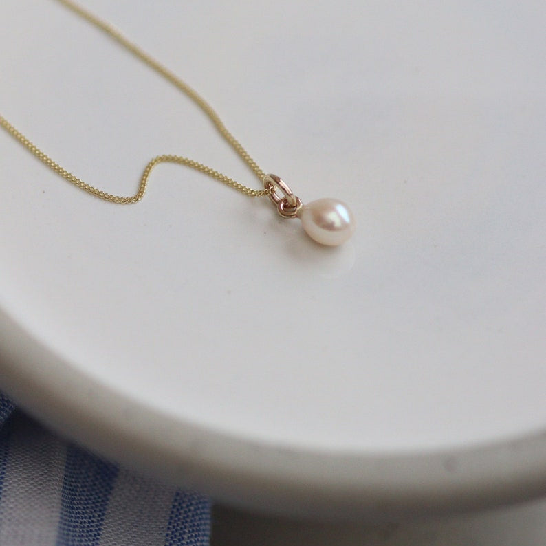 Pearl drop gold chain necklace on a white plate with a blue cloth underneath
