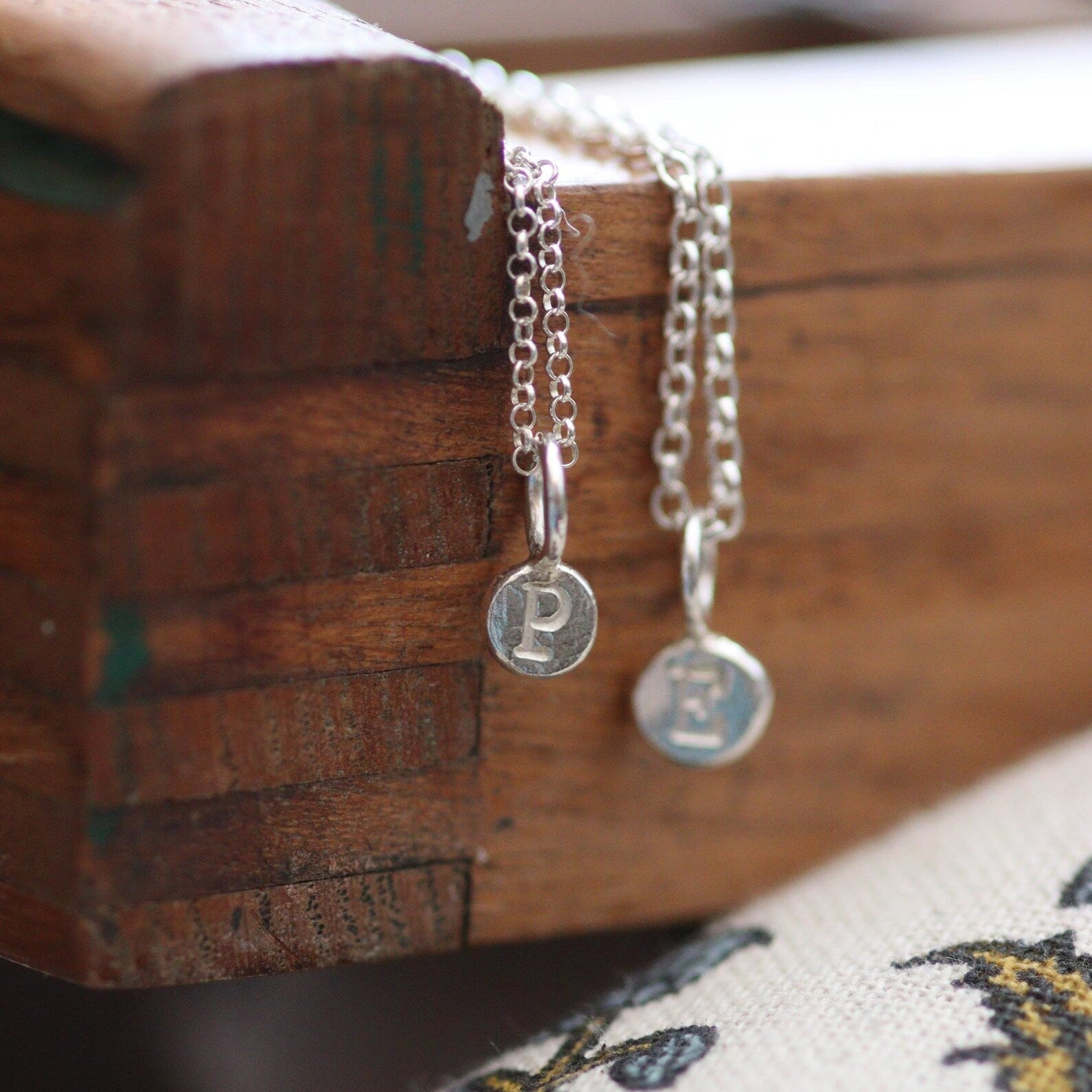 Silver pebble pendants on a silver chain against a wooden tray.