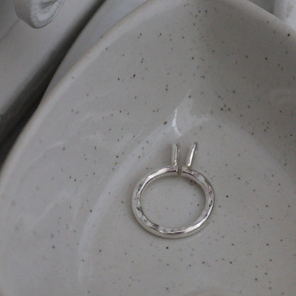 A silver keeper pendant with hammered finish on its own in a heart shaped bowl.