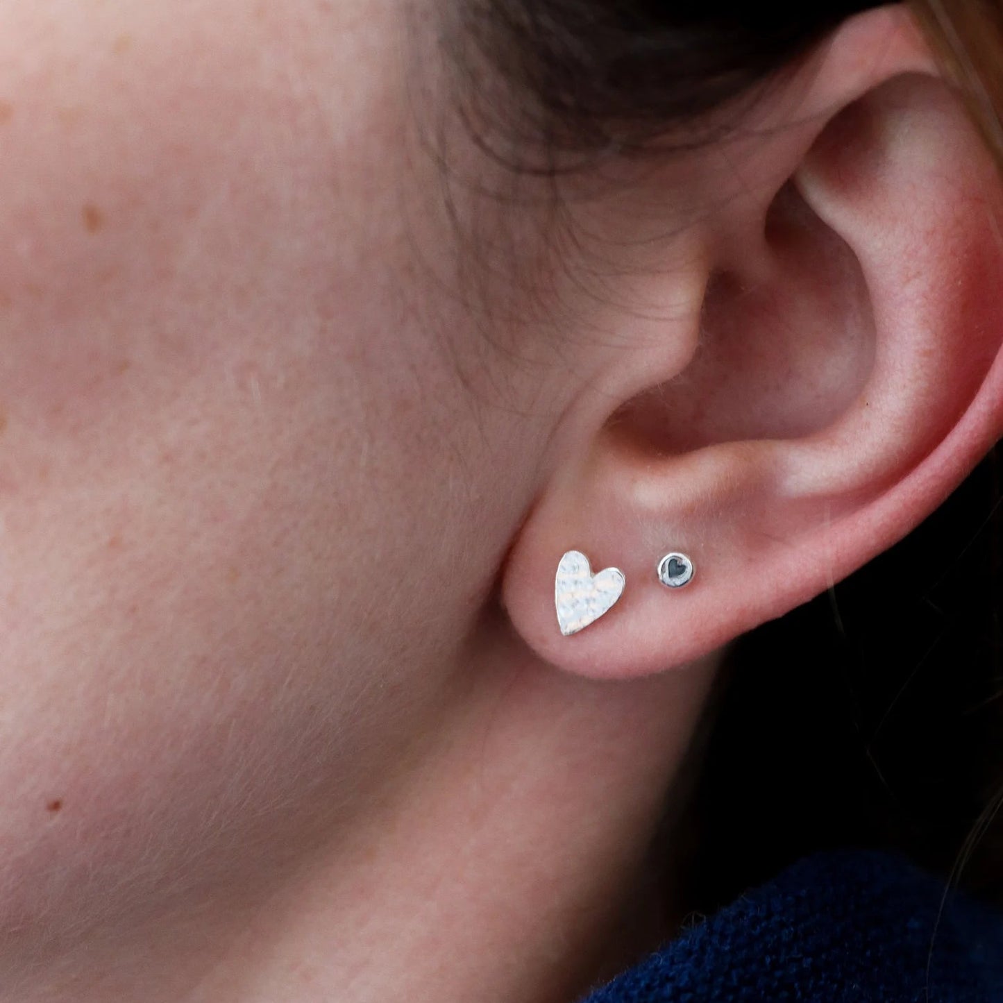 Close-up of an ear wearing two heart-shaped earrings with a blue garment in the background