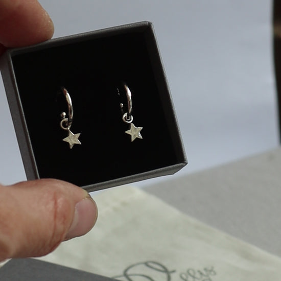 Silver hammered huggie hoops with star dangles in a grey branded jewellery box.