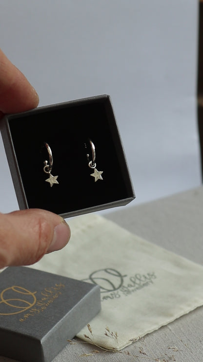 Silver hammered huggie hoops with star dangles in a grey branded jewellery box.