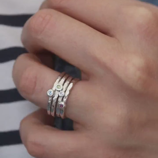 a set of hammered silver birthstone stacking rings on a model in a striped top and denim gilet.