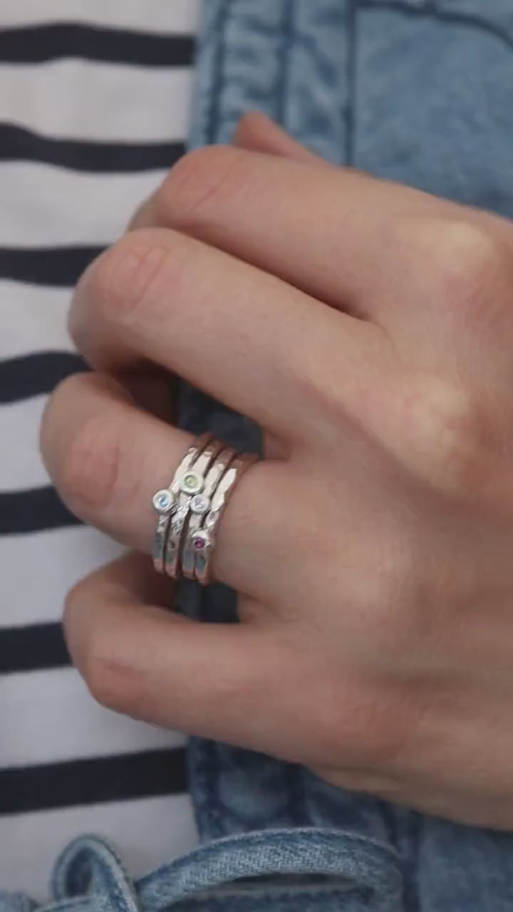 a set of hammered silver birthstone stacking rings on a model in a striped top and denim gilet.