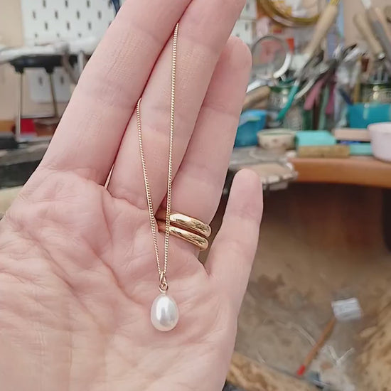 Handmade gold chain necklace with large pearl drop held in from of a jewellers bench