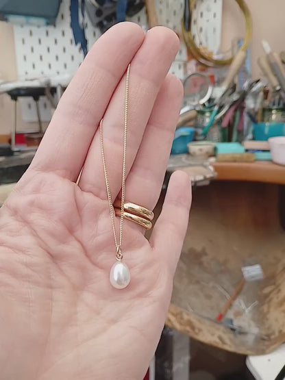 Handmade gold chain necklace with large pearl drop held in from of a jewellers bench