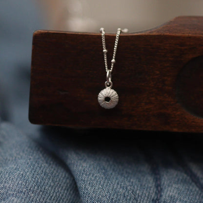 silver urchin charm on a beaded necklace draped over a drawer