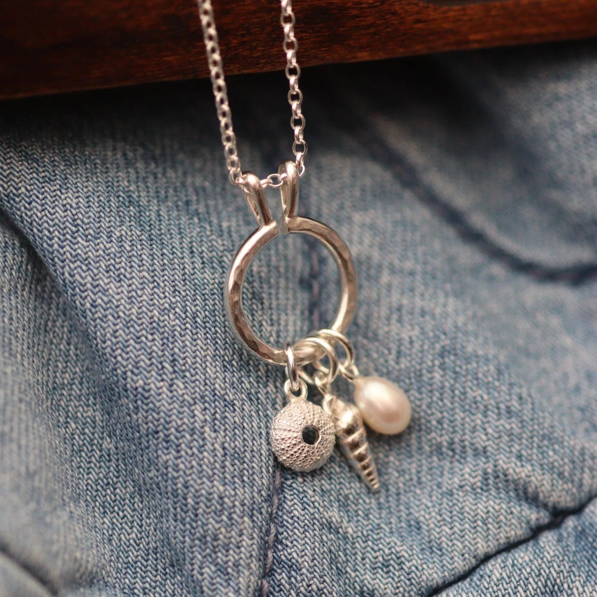 a silver keeper necklace with various charms including a pearl, spiral shell and sea urchin. It looks like a modern charm necklace.