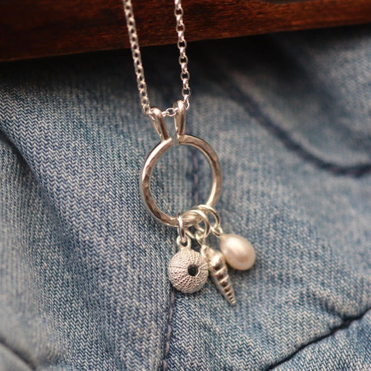 a silver keeper necklace with various charms including a pearl, spiral shell and sea urchin. It looks like a modern charm necklace.