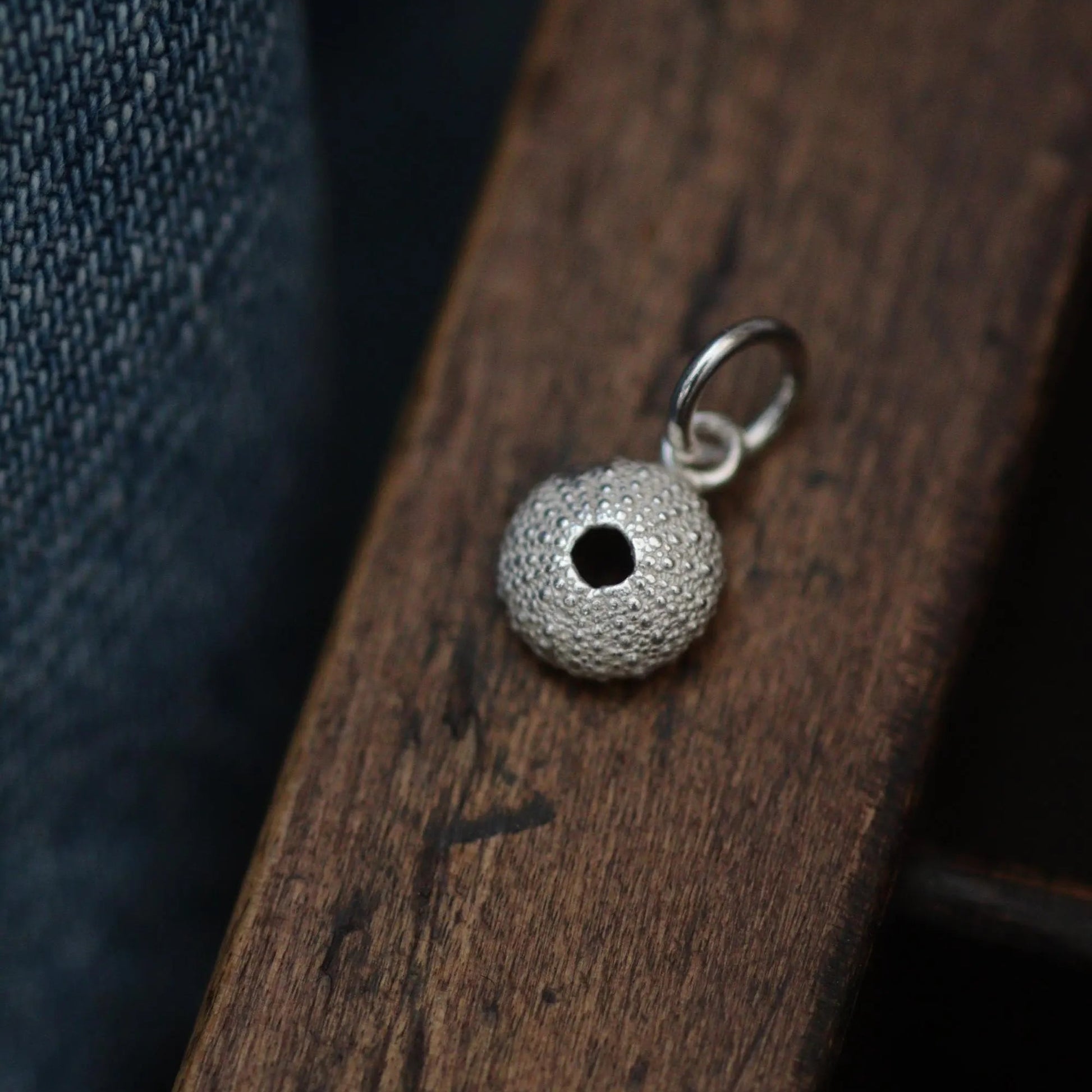 beautiful detail silver sea urchin charm on a wooden draw.