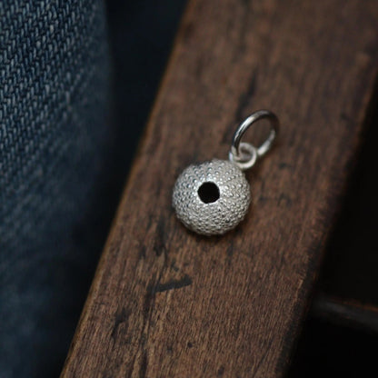 beautiful detail silver sea urchin charm on a wooden draw.