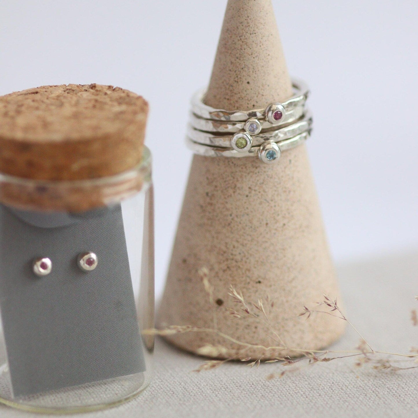 glass bottle containing silver studs and a ring cone with silver rings on a light gray background 