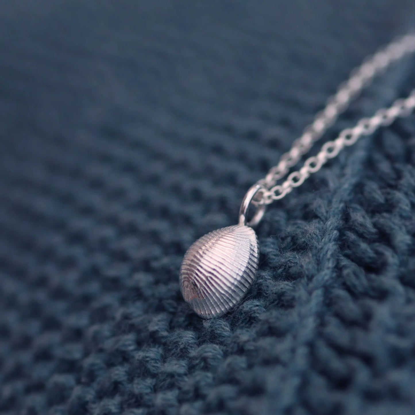 The back of a solid silver cowrie shell on a chain against a turquoise jumper