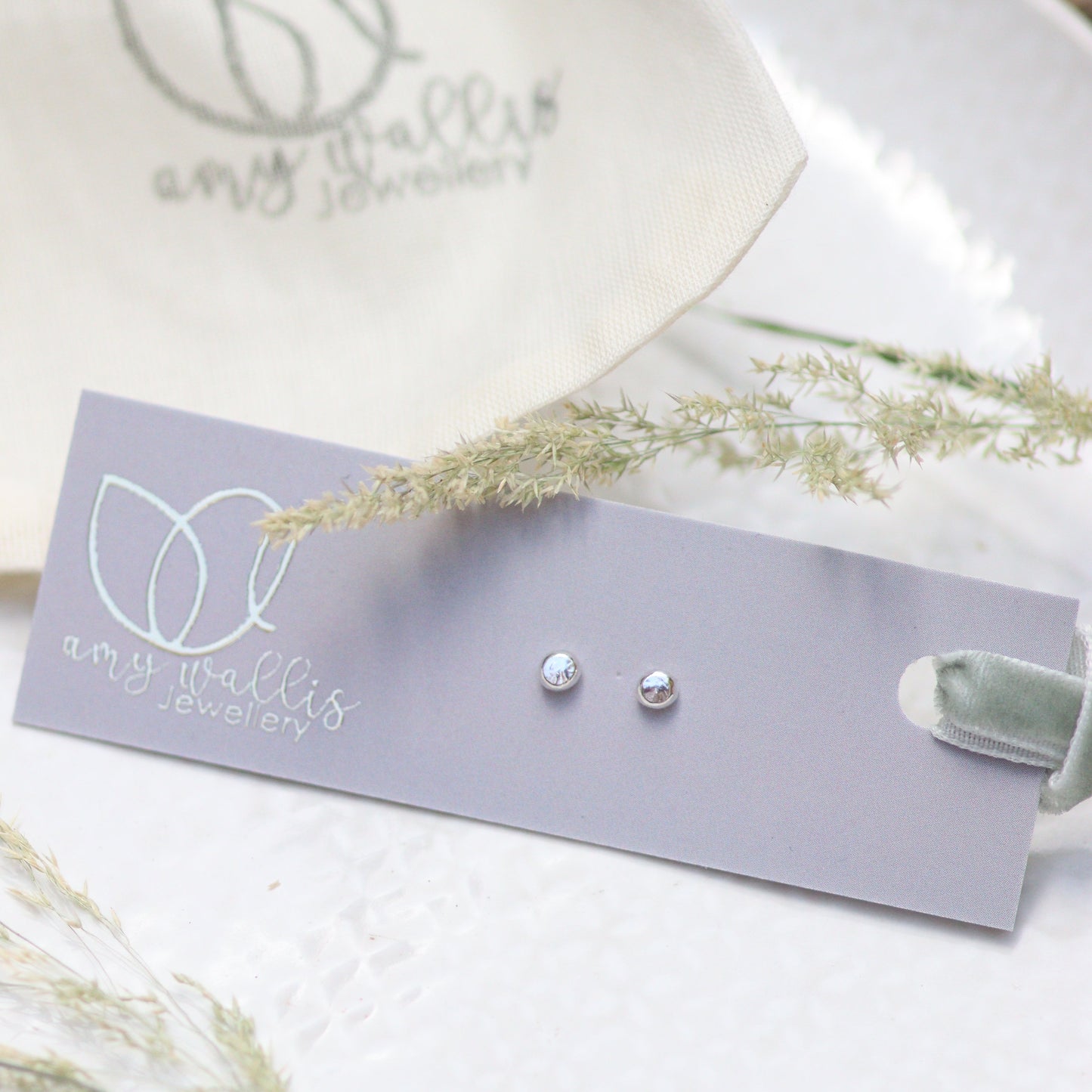 Pair of silver dot earrings on a grey card with a white background