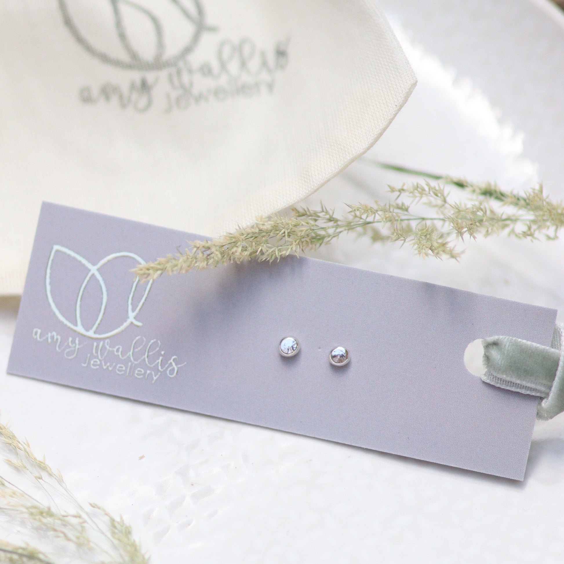 Pair of silver dot earrings on a grey card with a white background