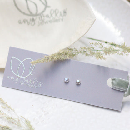 Pair of silver dot earrings on a grey card with a white background