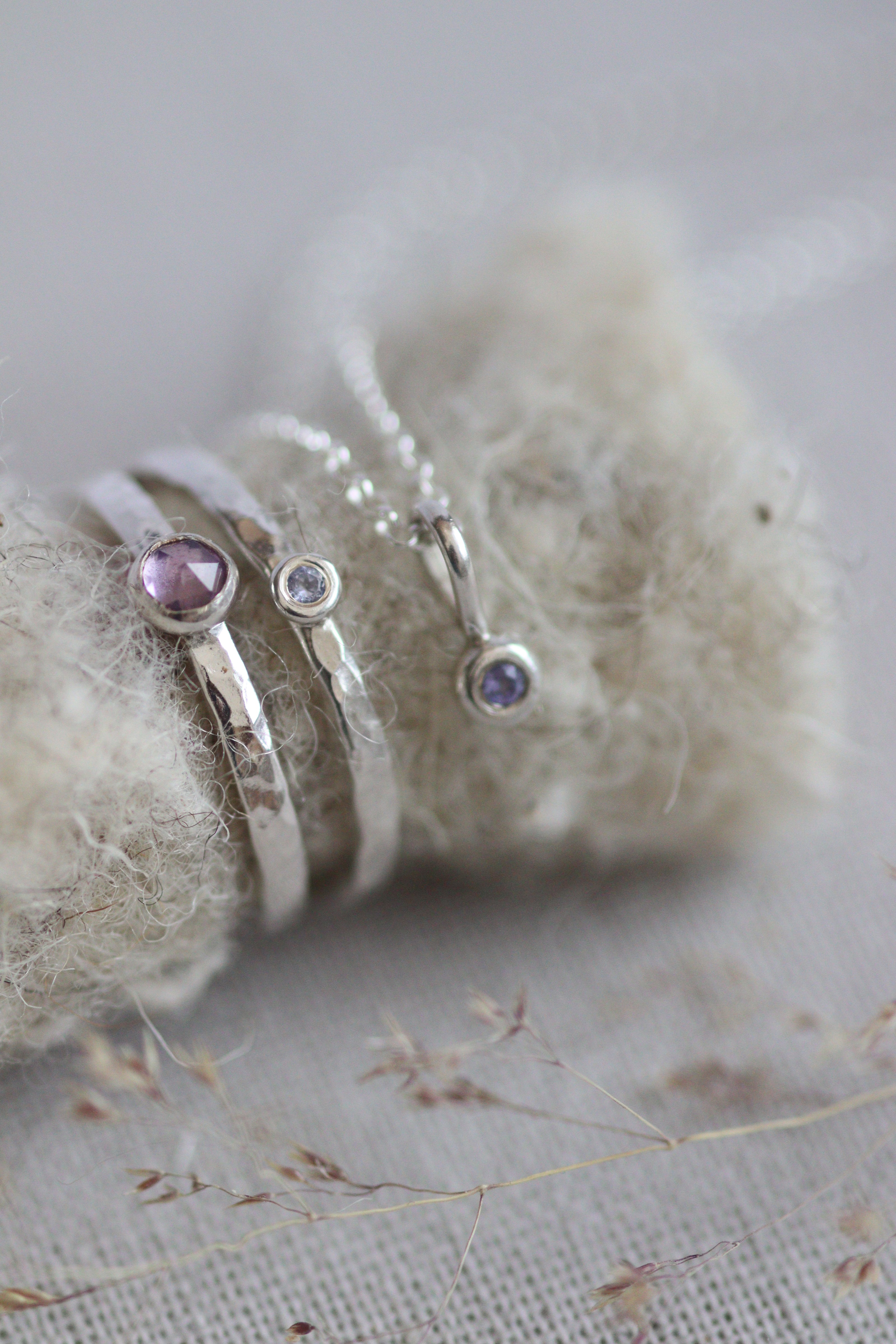 Silver rings set with amethyst and tanzanite purple stones next to a small pendant se with  a birthstone.