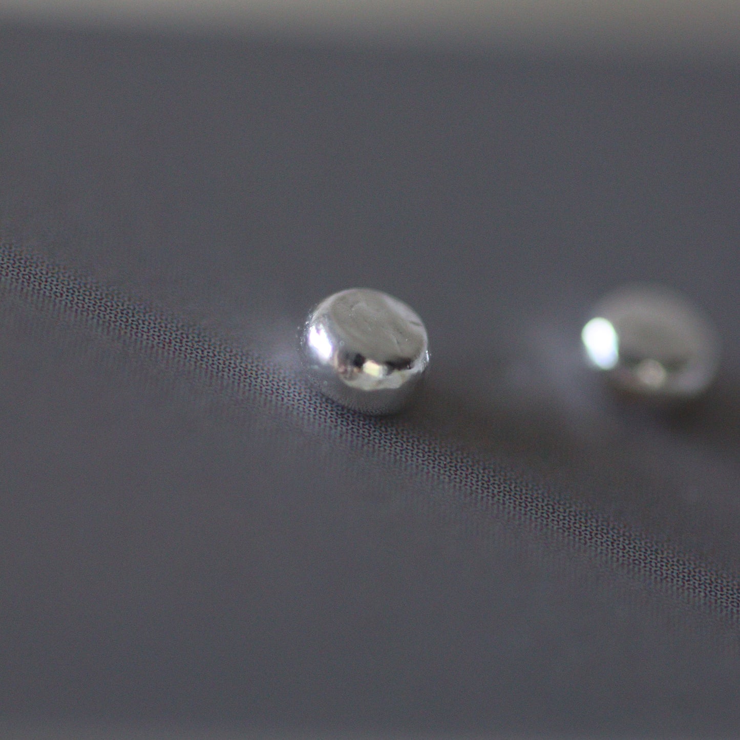 Close-up of three silver stud earrings on a textured grey card background