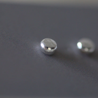 Close-up of three silver stud earrings on a textured grey card background