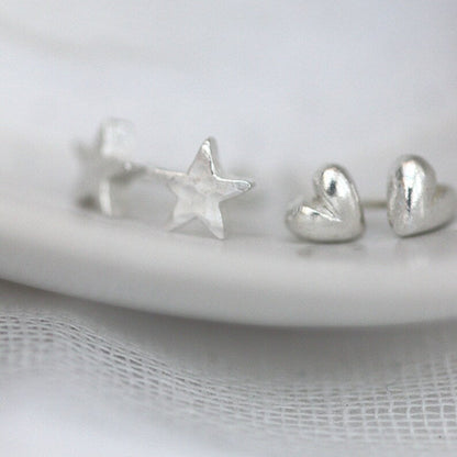 tiny silver heart and star studs next to each other on the edge of a plate, They are the same size.