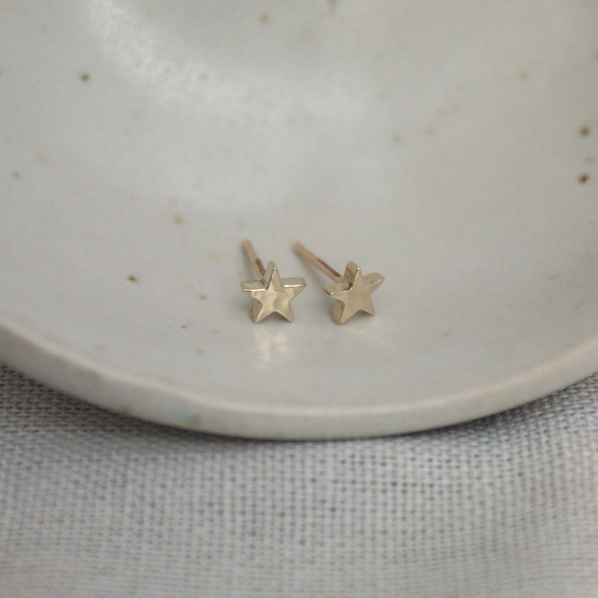 Little 9ct yellow gold star studs on a white bowl. The studs have a hammered finish.